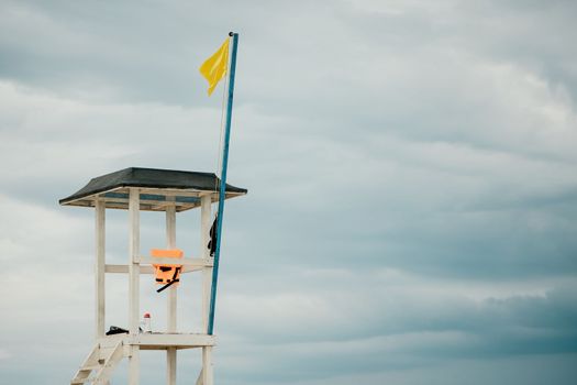 Empty white lifeguard tower with a yellow flag on the beach in windy weather. Beach lifeguard tower with yellow flag indicator. Nobody. Holiday recreation concept