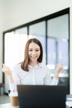 Excited businesswoman using computer laptop while in office, business concepts