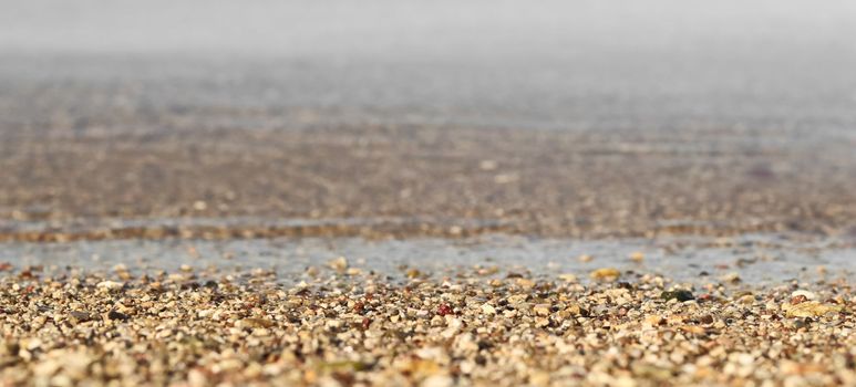 A background of sand, small pebbles and flowing wave on the sea beach. Summer vacation and coastal nature concept