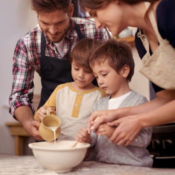 You boys are doing a great job. Two cute little boys baking with their parents in the kitchen