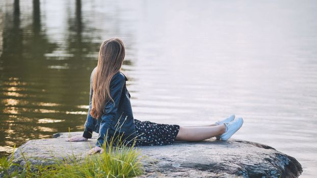 A girl sits by the lake on a rock