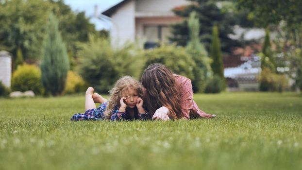 A mother and her daughter lie on the grass in the garden