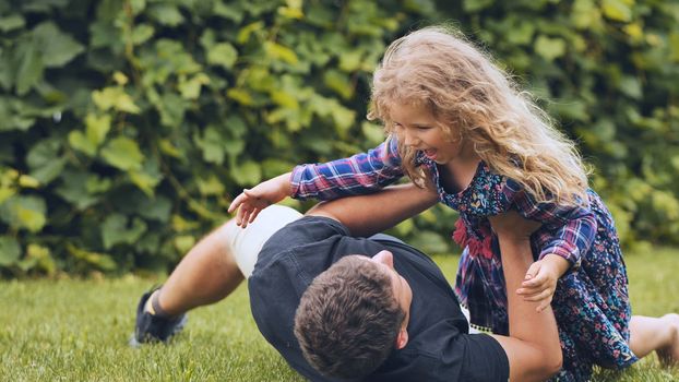A father plays with his daughter on the grass in the garden