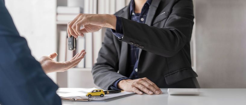 Car rental and Insurance concept, Young salesman giving car is key to customer after sign agreement contract with approved for rent or purchase...