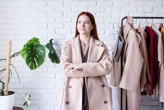 beautiful young woman in beige coat standing in front of hanger rack and choosing outfit dressing. Selection of a wardrobe, stylist, shopping. Clothes designing