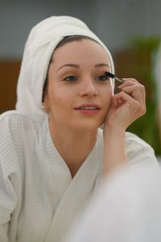 Attractive caucasian woman in bathrobe applying mascara on eyelashes. Beauty and cosmetics concept.