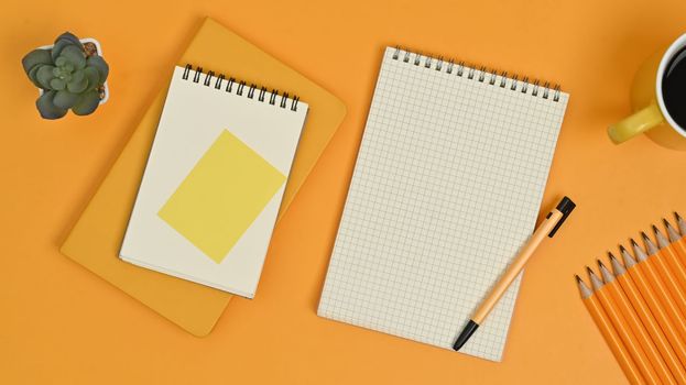 Top view of blank notepads, sticky note, pencils and coffee cup on yellow background.