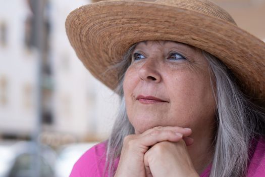 close-up of a woman with a hat and white hair in profile pensively looking at the horizon