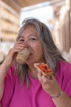 white-haired woman eating ham and tomato toast and coffee at a bar table