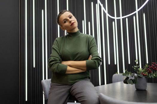 serious thoughtful business woman sits leaning on the table with her arms crossed over her chest.