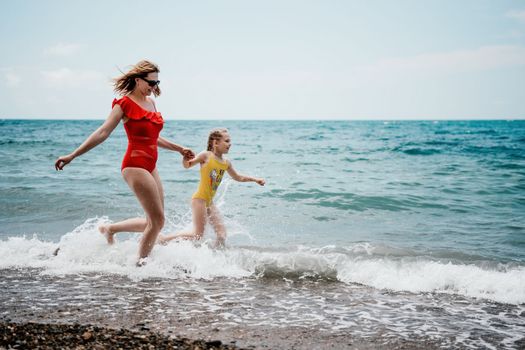 Happy loving family mother and daughter having fun together on the beach. Mum playing with her kid in holiday vacation next to the ocean - Family lifestyle and love concept.