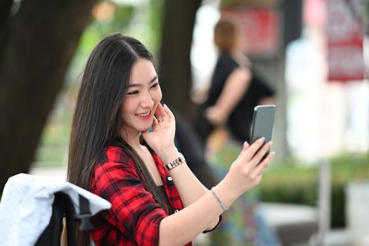 Young Asian woman having video call with her friends on smart while sitting outdoor in the city.