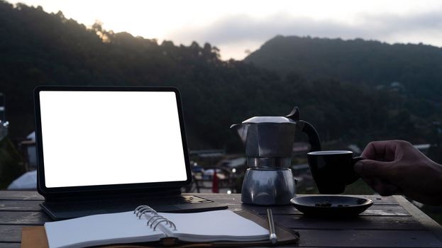 Computer laptop, notebook and coffee cup on wooden table with nature mountains view.