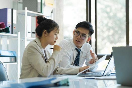 Businesspeople or colleagues are working together on investment project, discussing, sharing ideas, planning, and analyzing the business strategy and finance using laptop and graphs at workplace.