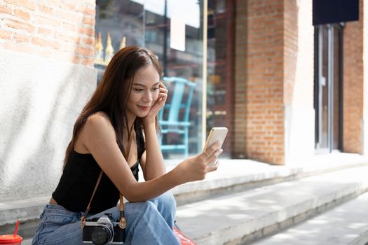 Cheerful Asian woman having video call on smart while sitting outdoor in the city.