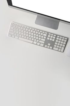 Overhead view computer with blank screen and wireless keyboard on white table.