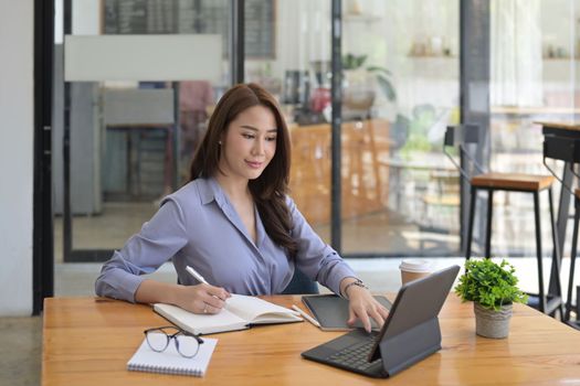 Beautiful businesswoman working with computer table and writing information on notebook.