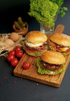 Homemade tasty double burger with beef, salad, bacon, tomatoes and cheese on wooden background. Rustic style.