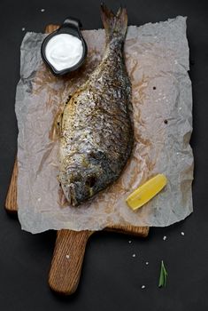 Roasted sea bream fish with herbs on a cutting board. Black background.