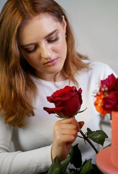 Portrait of a young woman in a white blouse holding a bouquet of roses on a pink background. Valentine's Day