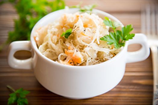 sauerkraut with carrots and spices in a bowl on a wooden table.
