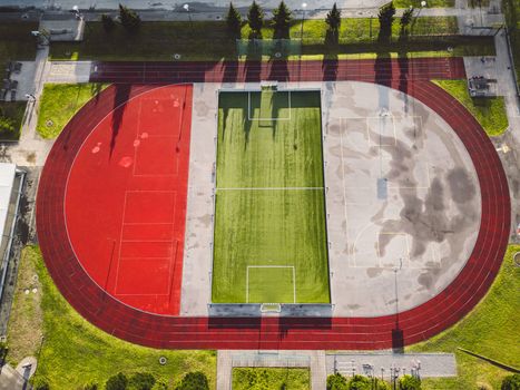 Aerial view, directly above a stadium, with red race track and green field in the middle.