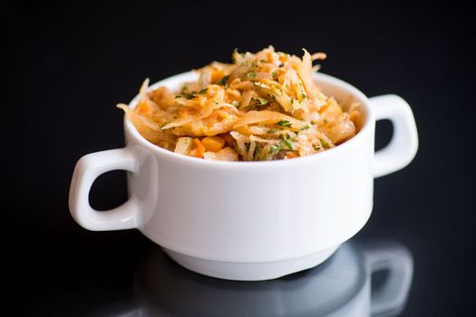 stewed cabbage with carrots and spices in a bowl on a black background.