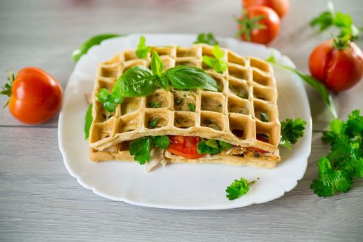 Sandwich of two egg omelettes with bacon and tomatoes inside, waffle shaped.