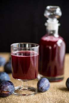 plum red wine in a glass and a decanter against the background of ripe large plums on the table.