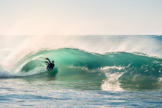 man surfing rides in the barrel of a beautiful wave that breaks with energy and power, sunlight reflects golden on the turquoise surface of the sea and in the foam, the wind rises columns of water