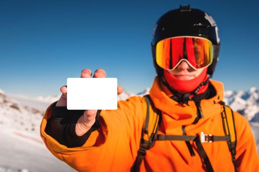 Snowboarder or skier holding blank lift pass in hand, portrait with mountain in the background. Ski pass in hand close-up.