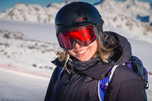 woman with a beautiful smile in a ski helmet. Portrait of a female skier in a safe ski helmet and goggles against the backdrop of picturesque snow-capped mountains. Active people leisure concept image.