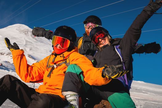 Laughing friends on winter vacation with skiing in snowy mountains, looking at camera. A company of people is enjoying a winter holiday in a ski resort.