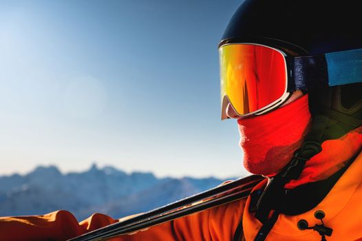 Portrait of a skier in profile in ski goggles against a clear blue sky and mountains.