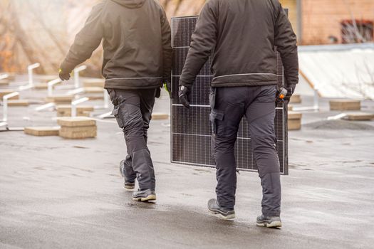 The process of installing solar panels. Solar panel installers work on the roof. Installers carry solar panel module to installation site, green and renewable energy concept.