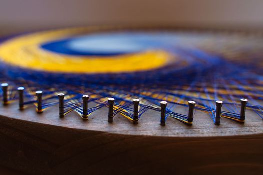 Colored thread mandala on a wooden board with nails. Mandala Moon Harmony Sun esotericism and psychology pictures from yellow and blue silk threads