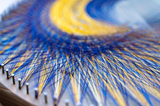 Colored thread mandala on a wooden board with nails. Mandala Moon Harmony Sun esotericism and psychology pictures from yellow and blue silk threads