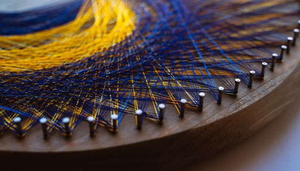 Colored thread mandala on a wooden board with nails. Mandala Moon Harmony Sun esotericism and psychology pictures from yellow and blue silk threads