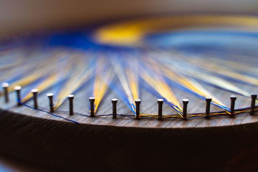 Colored thread mandala on a wooden board with nails. Mandala Moon Harmony Sun esotericism and psychology pictures from yellow and blue silk threads