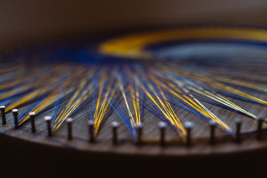 Colored thread mandala on a wooden board with nails. Mandala Moon Harmony Sun esotericism and psychology pictures from yellow and blue silk threads