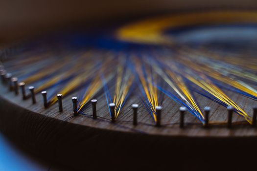 Colored thread mandala on a wooden board with nails. Mandala Moon Harmony Sun esotericism and psychology pictures from yellow and blue silk threads