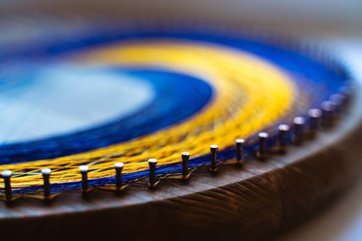 Colored thread mandala on a wooden board with nails. Mandala Moon Harmony Sun esotericism and psychology pictures from yellow and blue silk threads