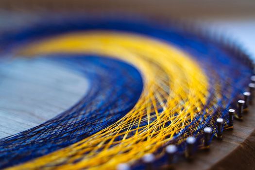 Colored thread mandala on a wooden board with nails. Mandala Moon Harmony Sun esotericism and psychology pictures from yellow and blue silk threads