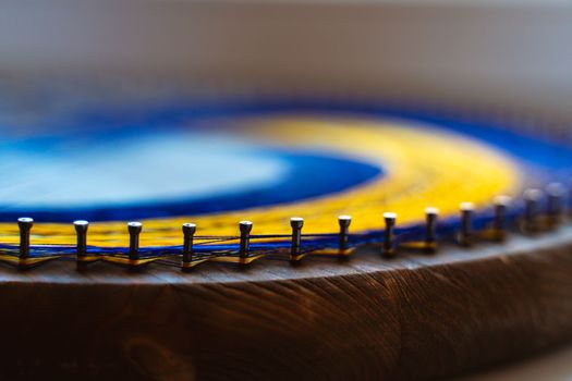 Colored thread mandala on a wooden board with nails. Mandala Moon Harmony Sun esotericism and psychology pictures from yellow and blue silk threads