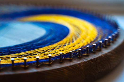 Colored thread mandala on a wooden board with nails. Mandala Moon Harmony Sun esotericism and psychology pictures from yellow and blue silk threads