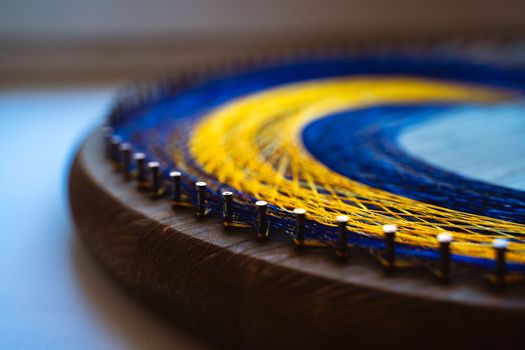 Colored thread mandala on a wooden board with nails. Mandala Moon Harmony Sun esotericism and psychology pictures from yellow and blue silk threads