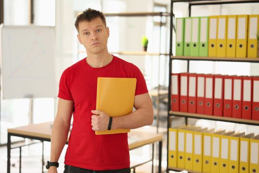 Surprised man with documents in hands in office with bookshelves and folders for papers. Paperwork concept