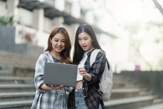 Beautiful young Asian woman college student with friends at outdoors. College student working on the college campus.