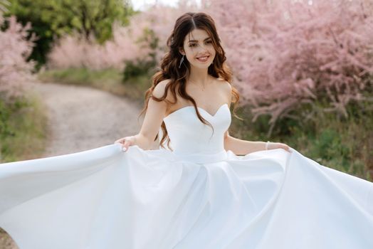 a young girl bride in a white dress is spinning on a path in a spring forest on a wedding day