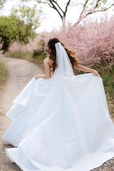 a young girl bride in a white dress is spinning on a path in a spring forest on a wedding day